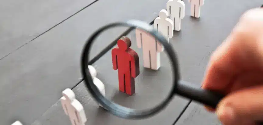 A magnifying glass is held over one red wooden figure